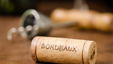 "A wine cork from Bordeaux France with a corkscrew, wine glass, and wine bottle in the background."